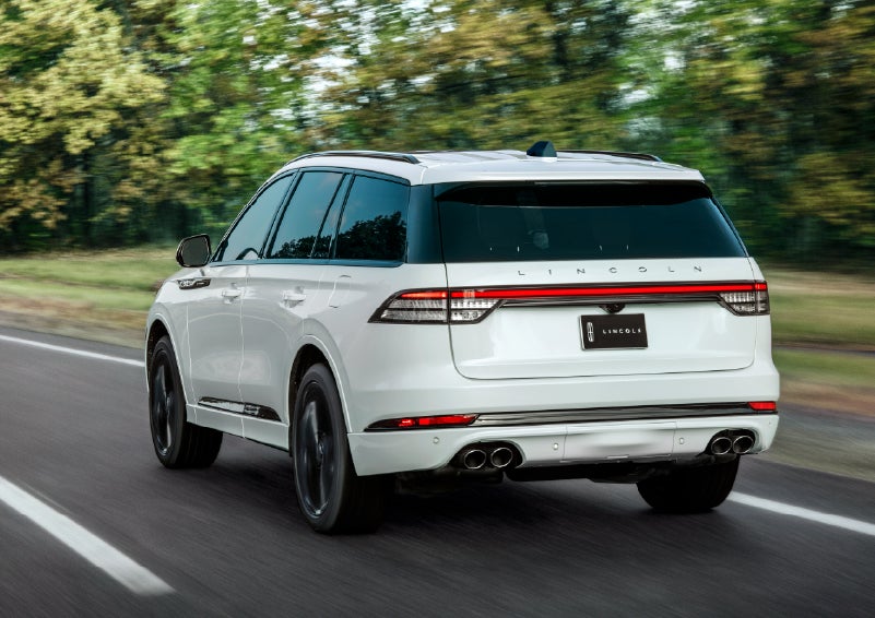 A white 2026 Lincoln Aviator® SUV is being driven away down a road lined with colorful trees. | Kirk Brothers Lincoln of Vicksburg in Vicksburg MS