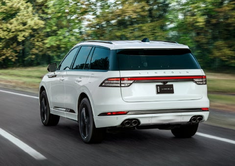 A white 2026 Lincoln Aviator® SUV is being driven away down a road lined with colorful trees. | Kirk Brothers Lincoln of Vicksburg in Vicksburg MS