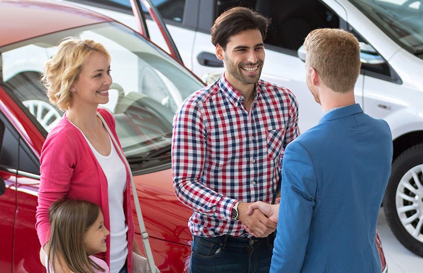 Family is happily smiling and a man is shaking hand with salesperson.